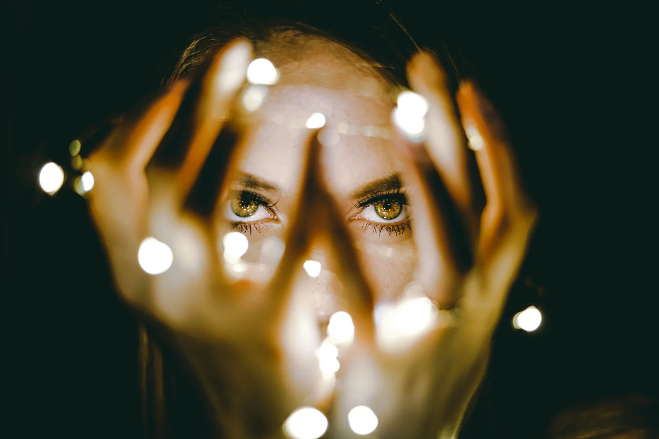 Face and hands with string lights in focus.